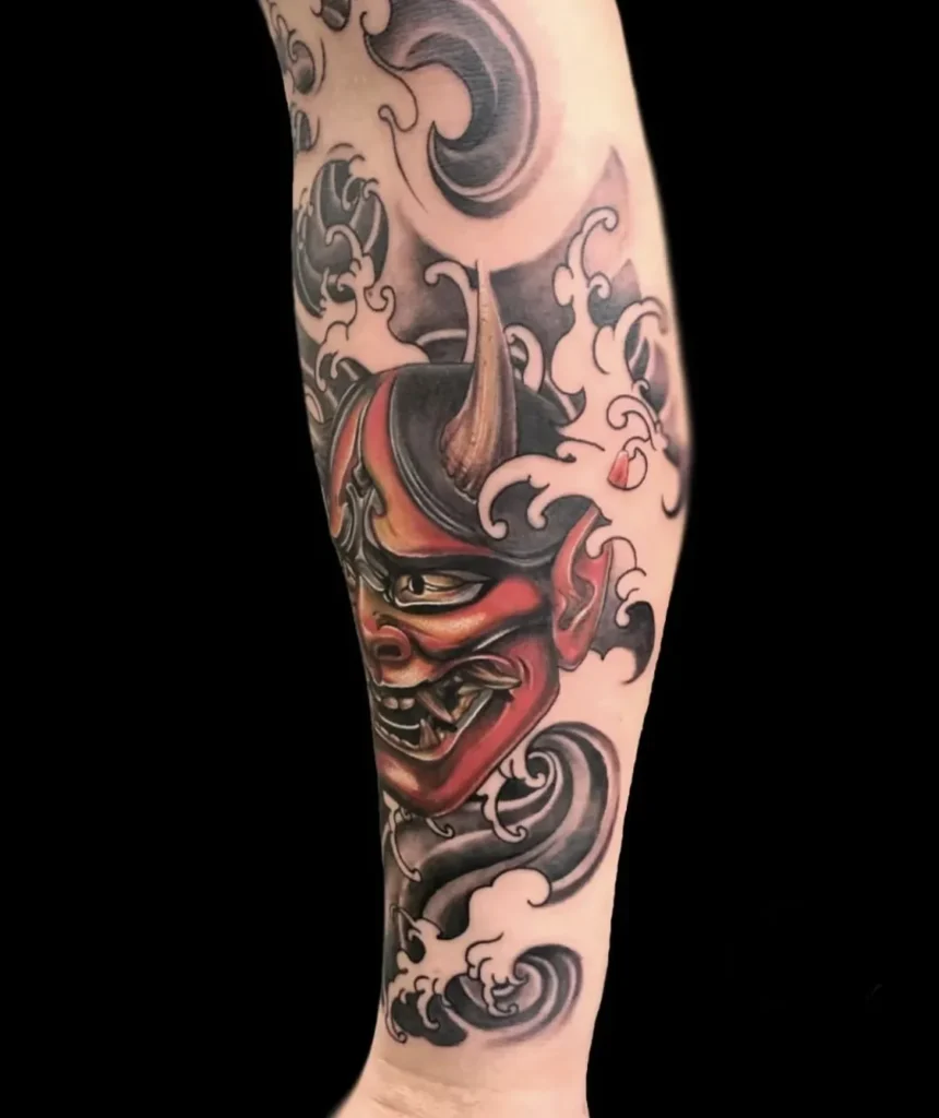 Tatuaje neoriental japonés a color de una máscara de oni rojo con cuernos entre olas, en el antebrazo